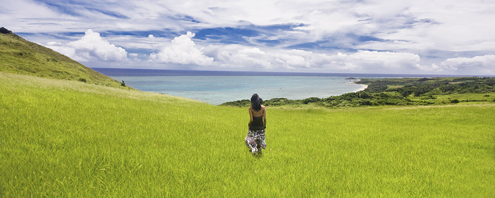Woman walking in grass near ocean --- Image by © Ocean/Corbis